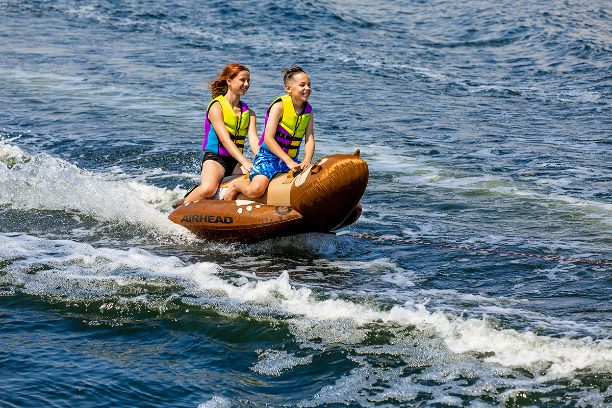 Bill's Exhausts Otter Riding Tube for water sports, orange inflatable towable tube with handles on a lake.