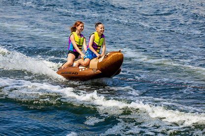 Bill's Exhausts Otter Riding Tube for water sports, orange inflatable towable tube with handles on a lake.
