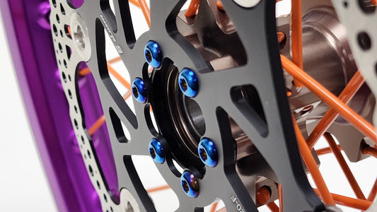 Warp9Racing Surron and Talaria Boost Spacer front rotor bolts shown on a motorcycle brake disc.