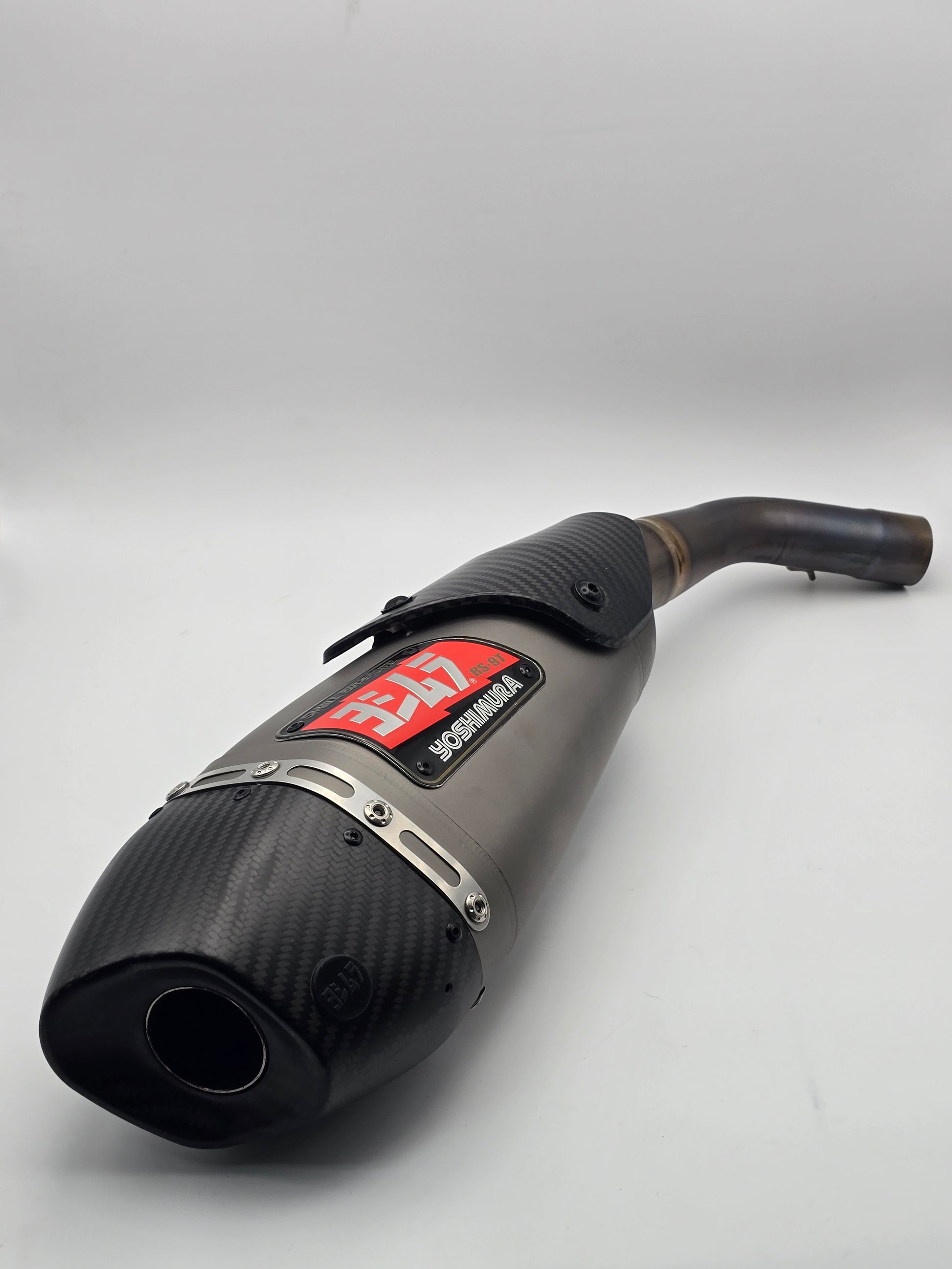 Used Yoshimura RS-9T titanium motorcycle exhaust system for Honda Grom 2014-2020, shown from the side with a sleek metallic finish.