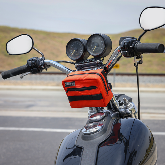Orange handlebar bag from THRASHIN SUPPLY CO. with secure straps and compact design for cycling storage.