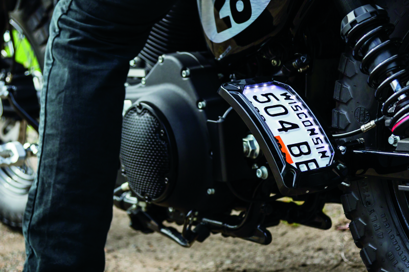 Kuryakyn Nova curved vertical mount side license plate holder in glossy black for motorcycle installation.