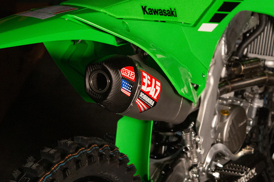 YOSHIMURA RS-12 exhaust system for Kawasaki KX250F motorcycle, showing the stainless steel muffler and mounting hardware.