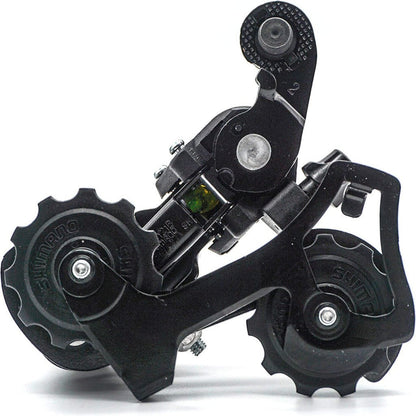 Shimano RD-TY21B bicycle rear derailleur for 6/7 speed bikes, mounted on a bike frame, showing gear adjustment mechanism.