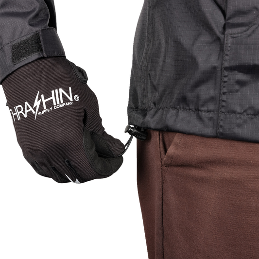 Black THRASHIN SUPPLY CO. Mission WP Rain Jacket in medium size, shown on a hanger with front zipper and hood.