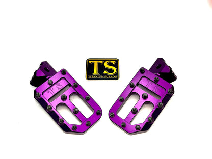 Titanium Surron custom foot pegs with titanium grips for Surron, Talaria, and Altis electric motos, shown with textured grip surfaces.