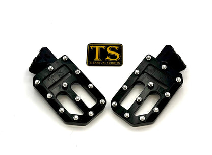 Titanium Surron custom foot pegs with titanium grips, designed for Surron and light e-moto bikes, shown mounted on the bike.