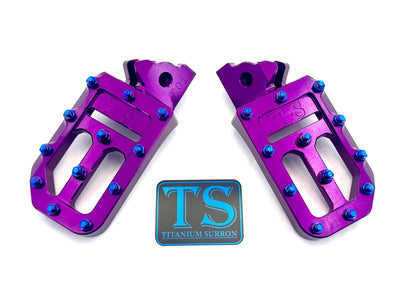Titanium Surron custom foot pegs with titanium grips for Surron and light e-moto bikes, featuring durable metallic texture.